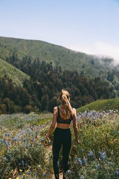 a woman walking down a trail in the mountains with wildflowers on both sides