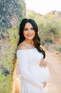 a pregnant woman leaning against a rock with her hands on her belly and smiling at the camera