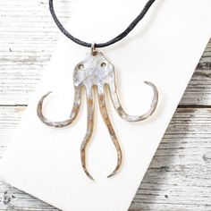 an octopus pendant is hanging on a white piece of paper next to a black cord