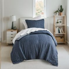 a bed with blue linens and pillows in a white room next to a window