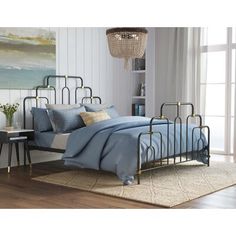 a metal bed frame with blue sheets and pillows on top of it in a room