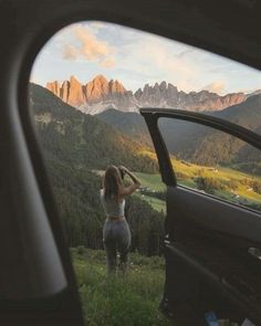 a woman standing in front of a car looking out the window at mountains and valleys