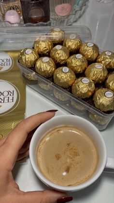 a person holding a cup of coffee next to some chocolates and a bag of candy