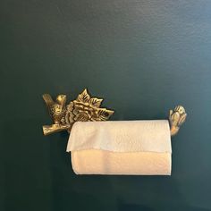 a gold toilet paper holder with two golden birds on it and a white towel hanging from the wall