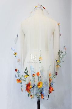 the back of a white dress with flowers on it and an embroidered letter is displayed