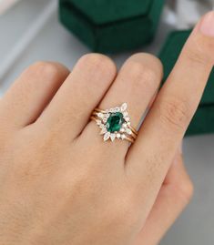 a woman's hand holding a ring with an emerald and white diamond in it