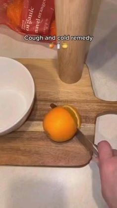 a person cutting an orange with a knife on a cutting board next to a bowl