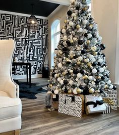 a white christmas tree with black and gold ornaments in a living room area next to a chair