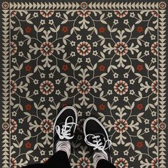 someone's feet in black and white shoes standing on a patterned rug with red flowers