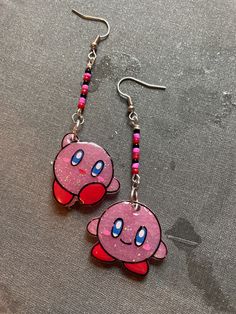 two pink and red earrings with blue eyes on them, sitting on a gray surface