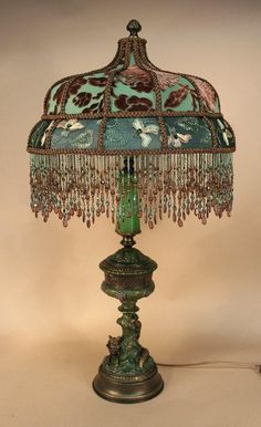 a green lamp on a white table with a brown base and blue glass beaded lampshade