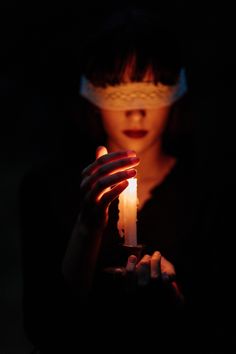 a woman holding a lit candle in her hands with the light shining on her face