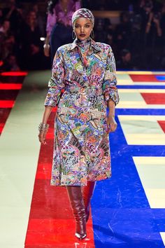 a model walks down the runway in a multicolored dress and knee high boots