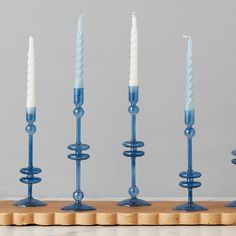 four blue candles are lined up in the same row on a wooden board with one white candle sticking out of it