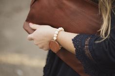 a woman wearing a brown leather handbag with a white beaded bracelet on her wrist