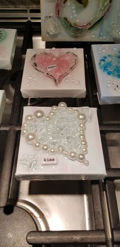 four square glass coasters sitting on top of a stove with pearls and other decorative items