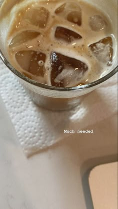 a glass filled with liquid and ice on top of a white table next to a cell phone