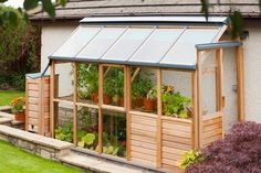 a small wooden greenhouse with plants growing in it's walls and windows on the side of a house