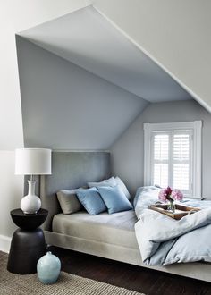 a bed sitting under a window next to a table with a vase on top of it