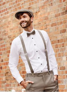 a man in a white shirt and bow tie standing next to a brick wall with his hands on his hips