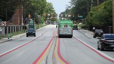 a green and white bus driving down a street next to tall buildings with traffic lights