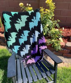 a black and blue blanket sitting on top of a wooden chair in the grass next to flowers