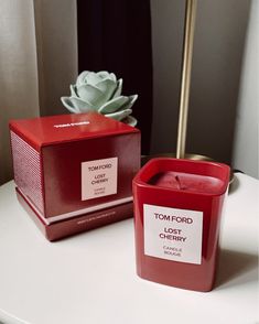 a red candle sitting on top of a white table next to a box with a plant in it