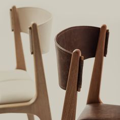 two chairs with wooden arms and leather seat covers, one in white and the other in brown