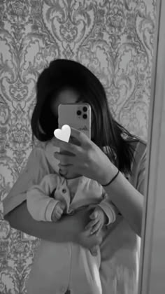 a woman taking a selfie in front of a mirror with her baby on her lap