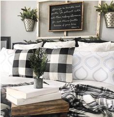 a bed with black and white pillows, plaid blankets and potted plants on it