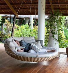 a woman laying on a hanging chair in the middle of a wooden floored porch