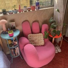 a pink chair sitting in front of a window next to a table with a potted plant on it