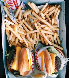 two cheeseburgers and fries in a box with french fries on the table next to them