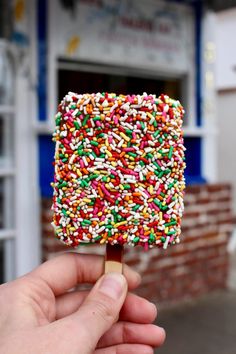 a hand holding a popsicle with sprinkles on it in front of a store