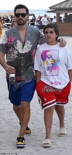 a man and woman walking on the beach with one holding his arm around the other