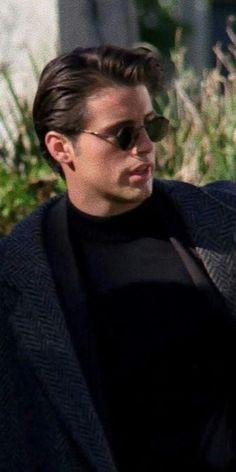 a young man wearing sunglasses and a black sweater looks off into the distance as he walks