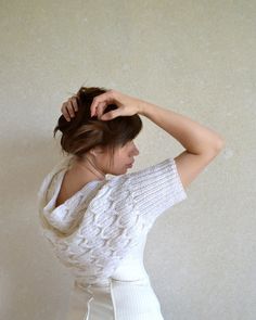 a woman wearing a white sweater and skirt with her hair in the air, standing against a wall