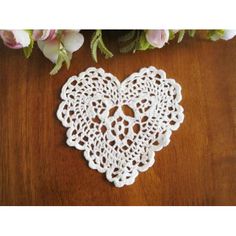 a heart shaped doily sitting on top of a wooden table next to pink flowers