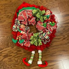 a christmas wreath on the floor with two elfs hanging from it's sides