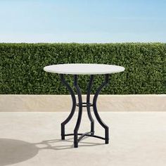 a white table sitting on top of a cement floor next to a green hedge covered wall