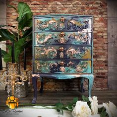 an old dresser with flowers and candles on the floor in front of a brick wall