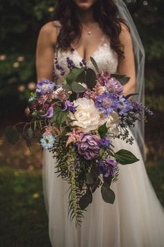 a bride holding a bouquet of purple and white flowers