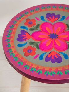 an artistically painted stool with wooden legs and flowers on the top, sitting on a white wood floor