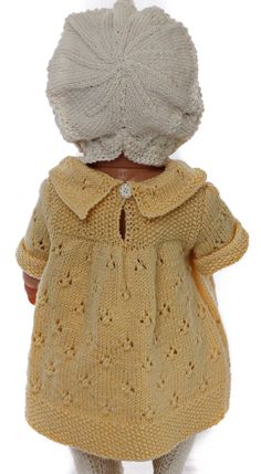 a doll wearing a yellow knitted dress and bonnet is standing in front of a white background