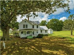 a white house sitting in the middle of a lush green field next to a tree