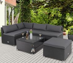 an outdoor patio furniture set with grey cushions and coffee table on a wooden deck surrounded by greenery