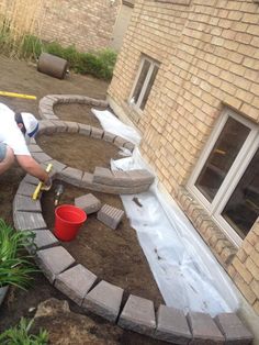 a man laying bricks on the ground in front of a house