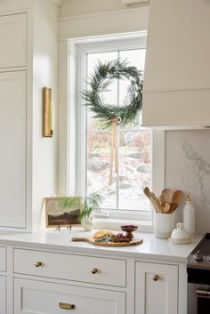 a kitchen with white cabinets and a wreath on the window sill