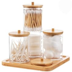 three glass jars with wooden lids and toothpicks in them on a wood tray