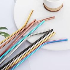 there are many different colored straws next to a white plate with a cup on it